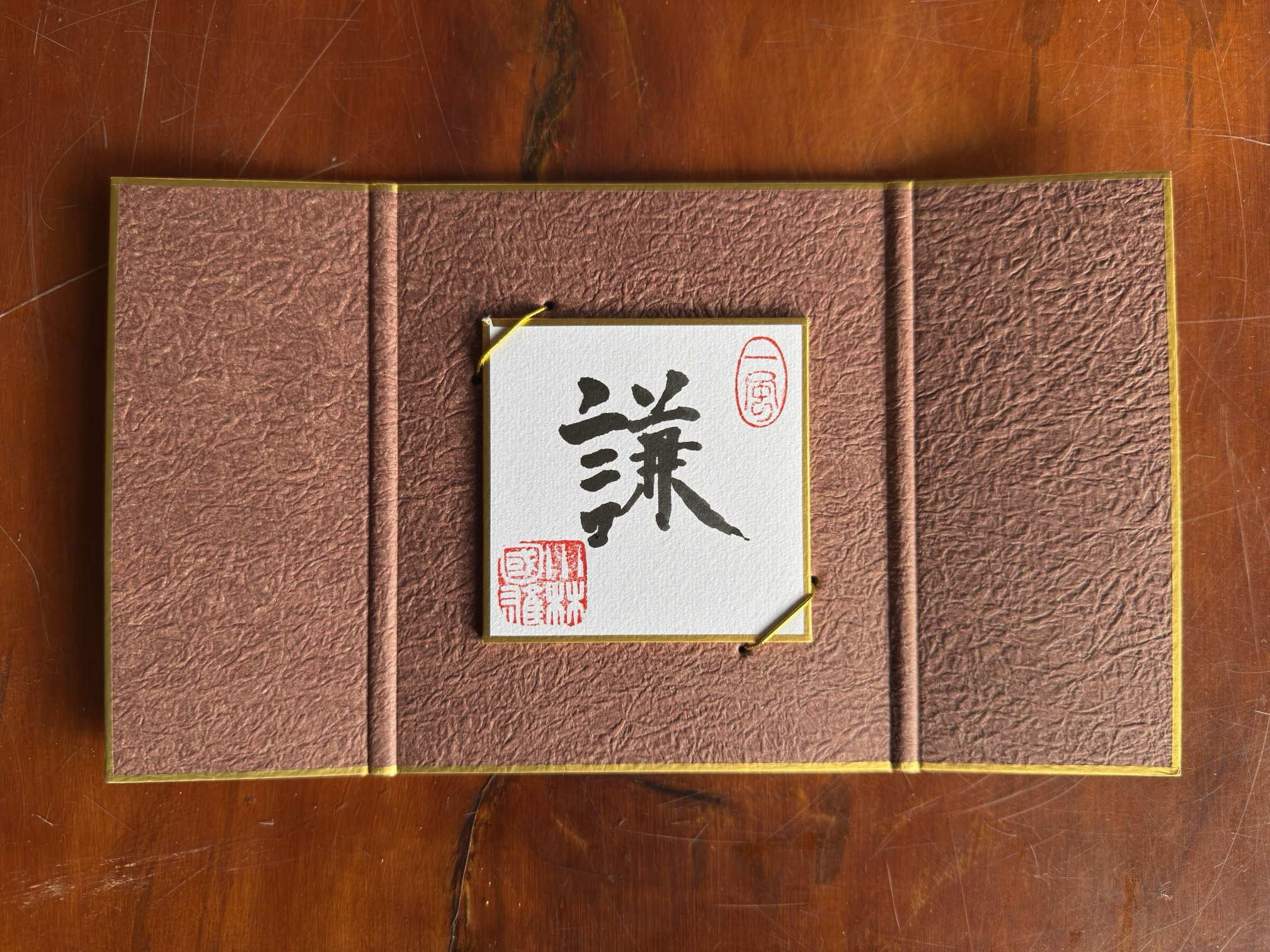 Shikishi con el kanji 謙 en un estuche plegable de papel washi