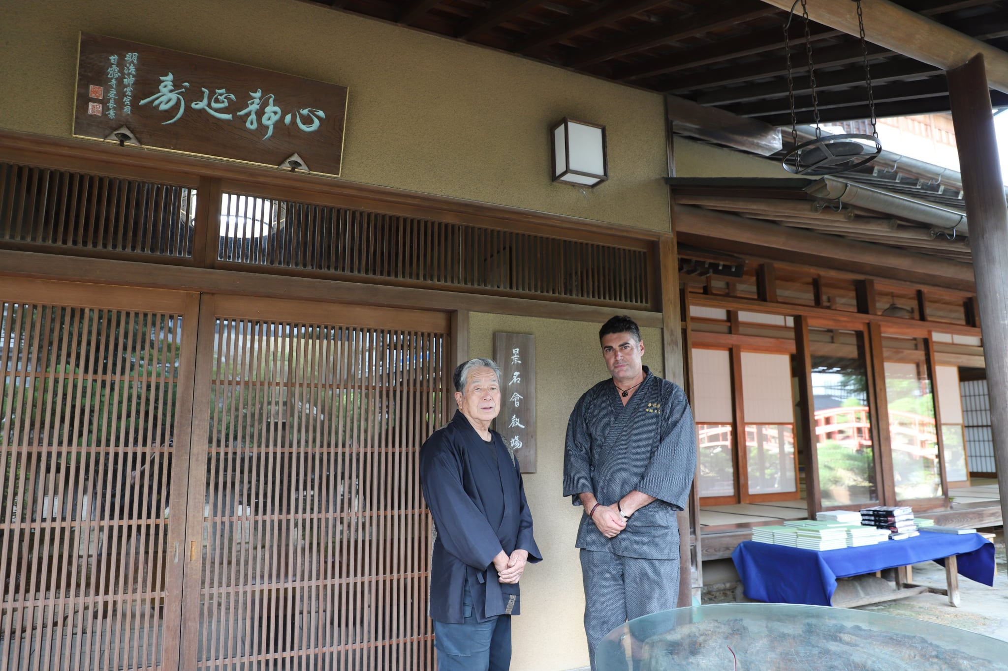 El III Iemoto Kobayashi Ippū y Masaru Ken ante la entrada de su casa, junto al rótulo de madera tallada de la escuela