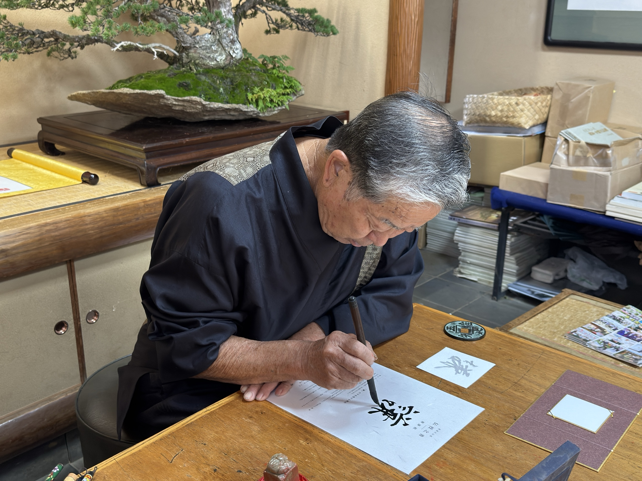 El III Iemoto Kobayashi Ippū traza a pincel el carácter 謙 sobre el documento de transmisión