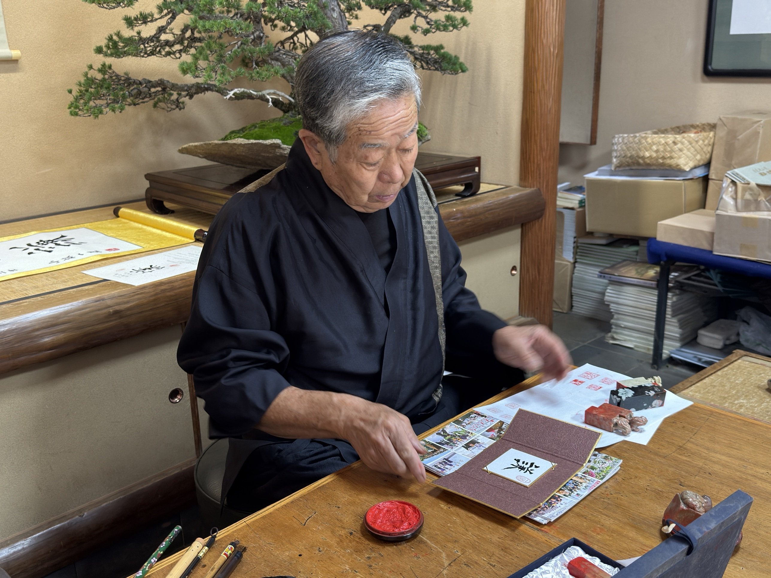 El III Iemoto Kobayashi Ippū prepara el estuche plegable del shikishi 謙, con el tampón de tinta roja y los sellos sobre la mesa
